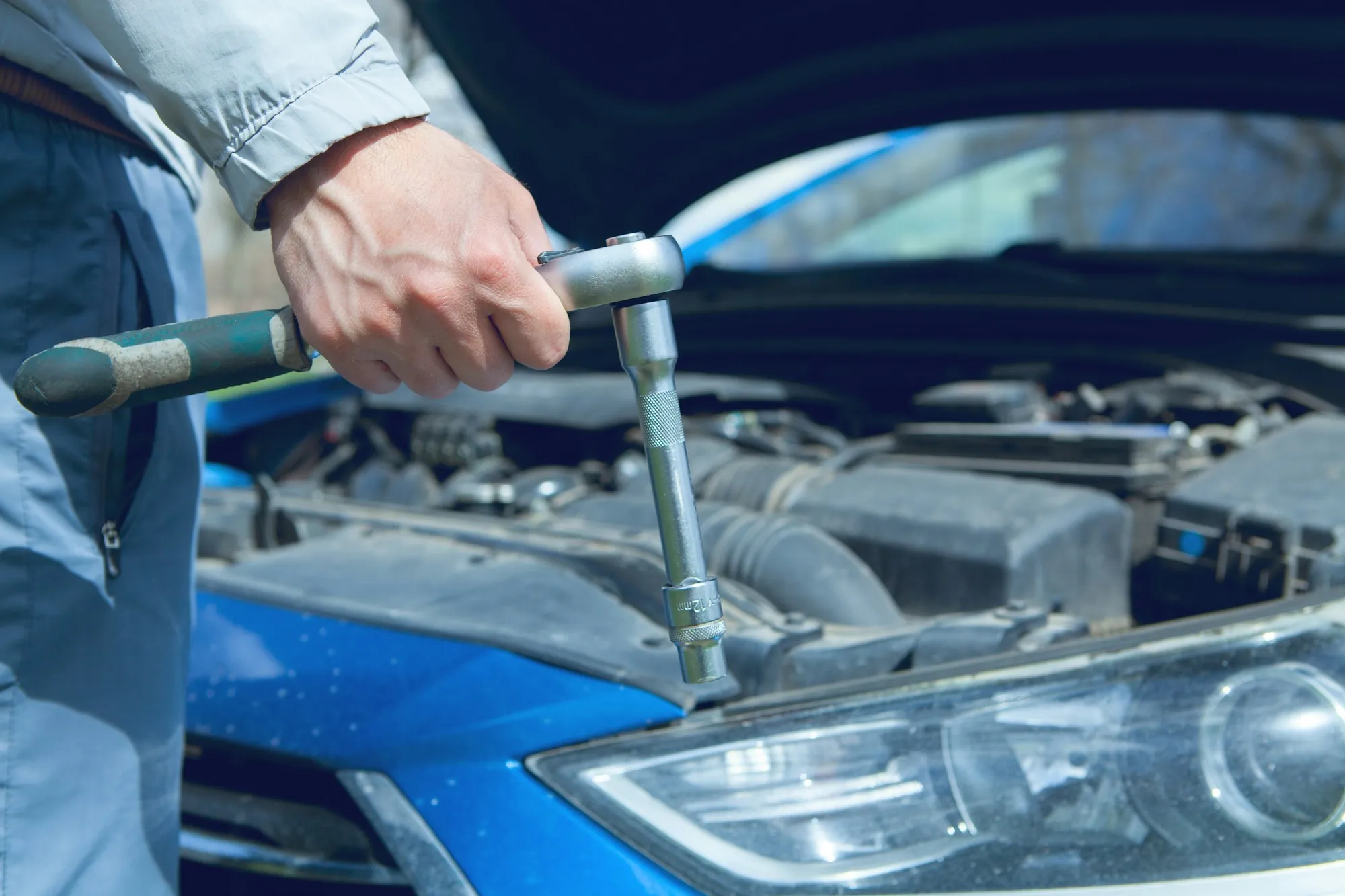 Mechanic using a wrench on a car engine with the hood open