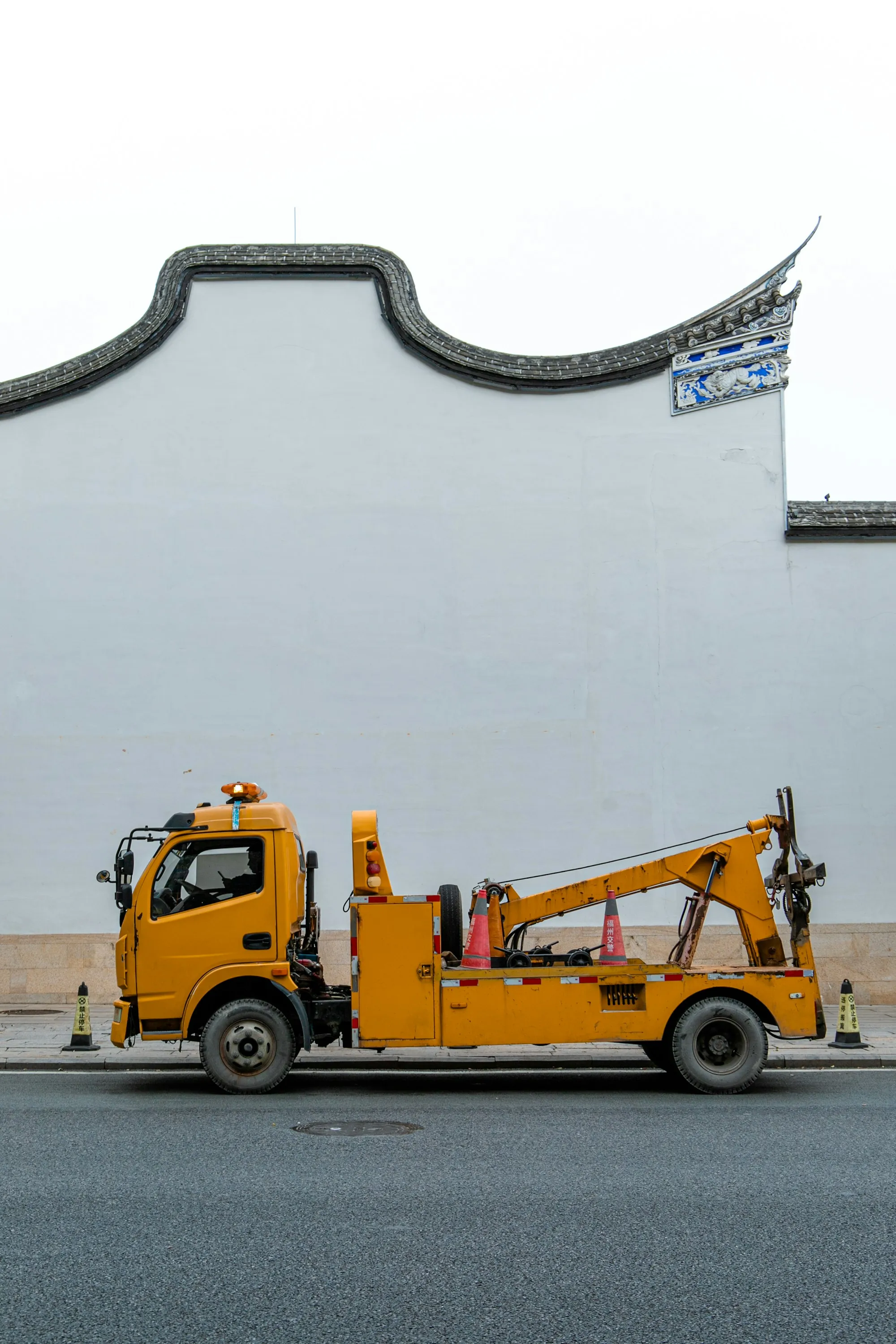 Yellow wrecker tow truck with a red boom parked by a white wall