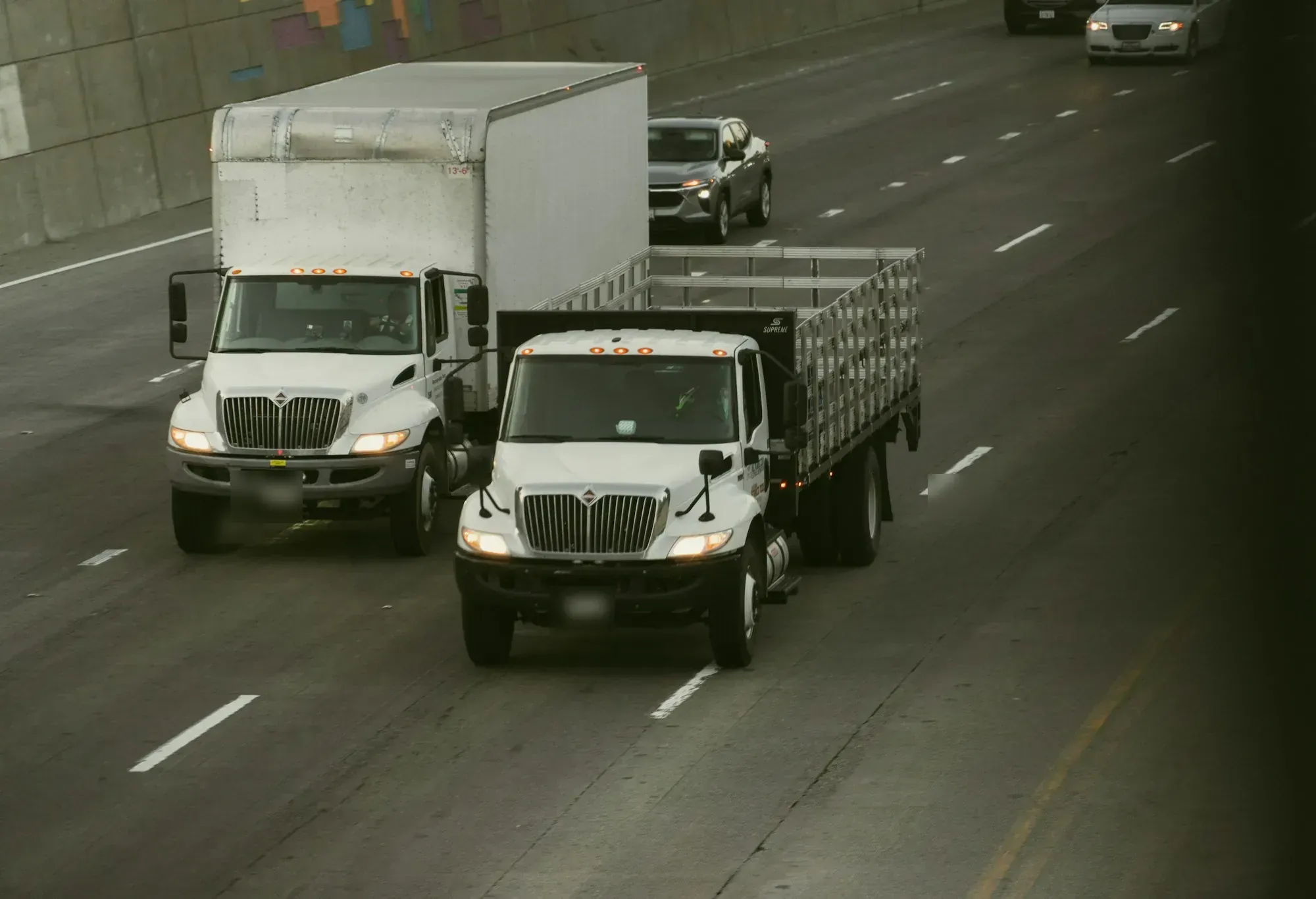 Two white work trucks driving in the right lanes of a multi-lane highway