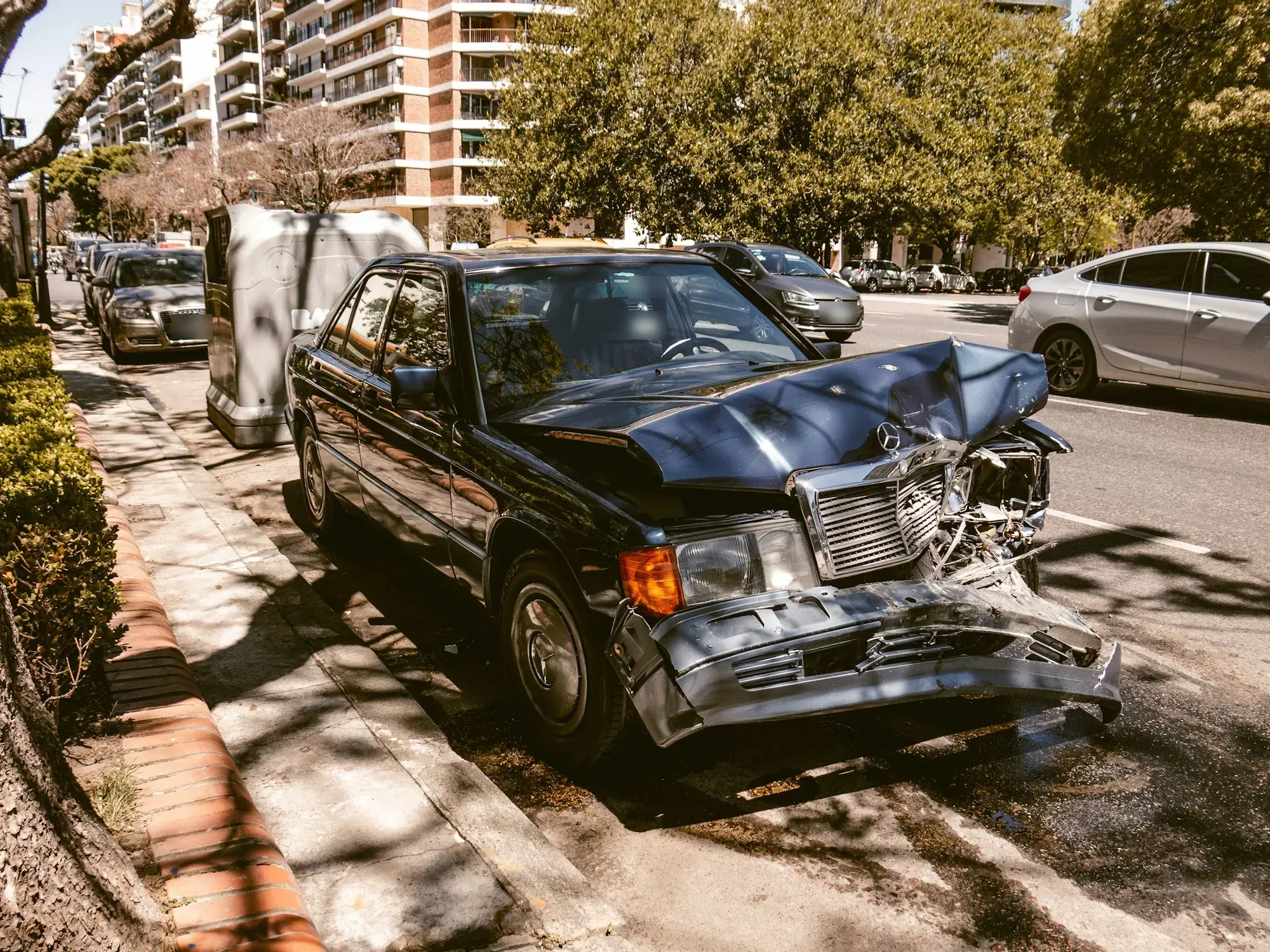 Black sedan with a crushed front end parked at a city curb after a crash