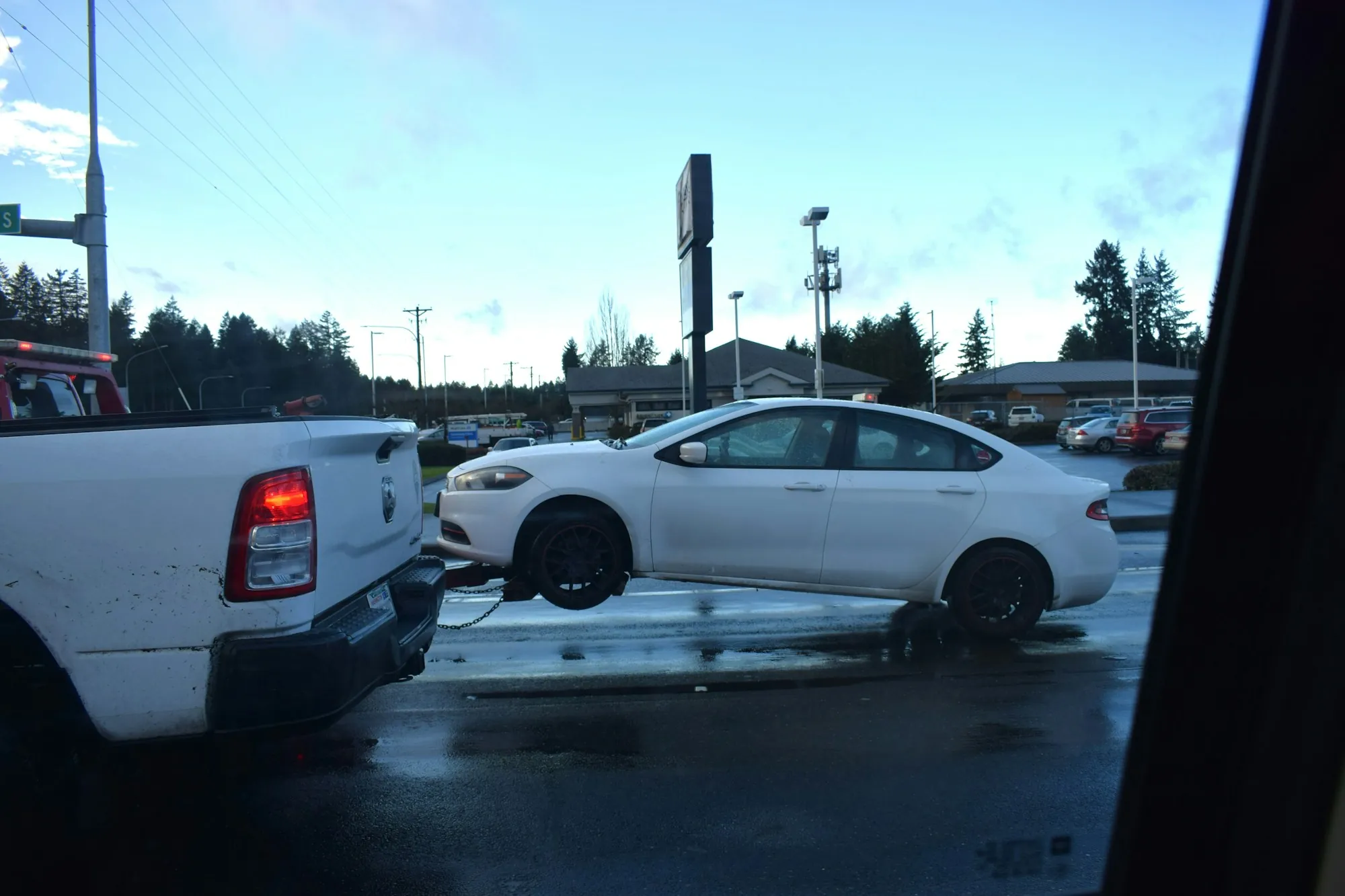 White sedan lifted onto the back of a tow truck in a rainy parking lot